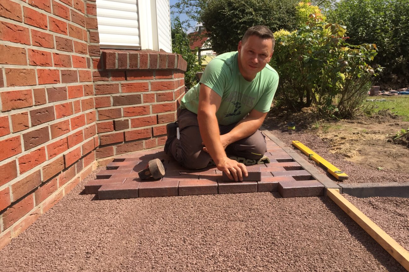 Ein Handwerker beim Pflastern einer Terrasse mit Rotklinker